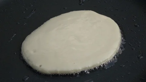 Slow motion of sizzling batter cake on hot dark gray fry pan close up. Stock Footage 100235522