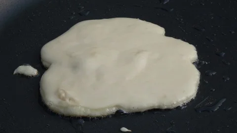 Slow motion of sizzling batter cake on hot dark gray fry pan with seed oil. Stock-Footage 100235779