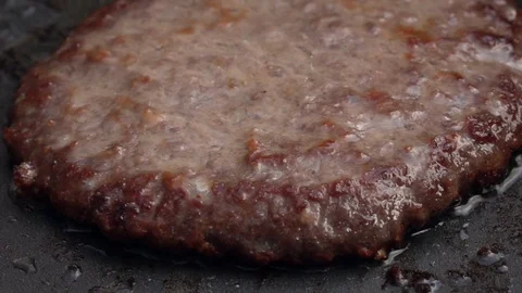 Slow motion of sizzling hamburger on dark gray fry pan close up. Stock Footage 99854914
