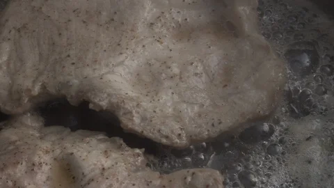 Slow motion of sizzling pork steaks on dark gray fry pan with glass lid. Stock Footage 99852273