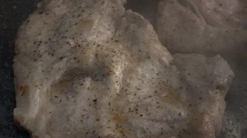 Slow motion of sizzling pork steaks on dark gray fry pan close up. Stock Footage 99852904