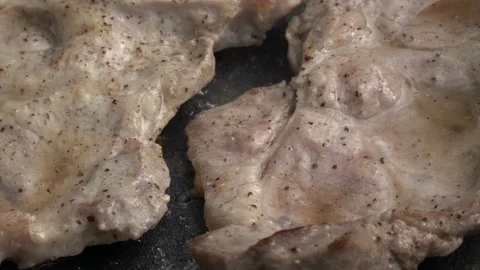 Slow motion of sizzling pork steaks, rotating on dark gray fry pan close up. Video stock 99852957