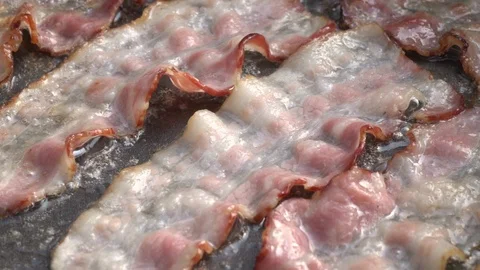 Slow motion of sizzling sliced bacon on dark gray fry pan close up. Stock Footage 99851774
