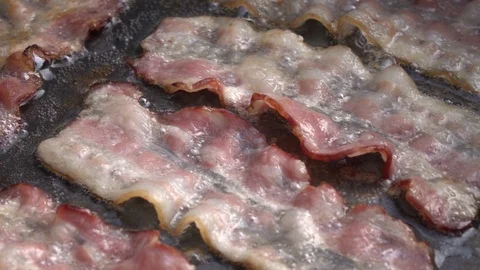 Slow motion of sizzling sliced bacon on dark gray fry pan, rotating close up. Stock Footage 99851811