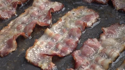 Slow motion of sizzling sliced crispy bacon on dark gray fry pan close up. Stock Footage 99851851
