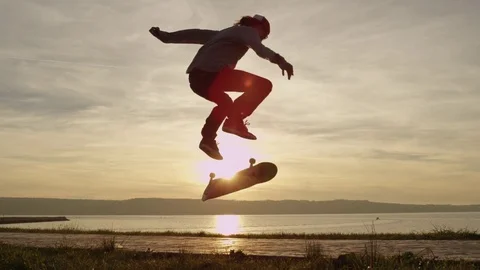 SLOW MOTION Skateboarder skating and jumping kickflip trick over the setting sun Stock Footage