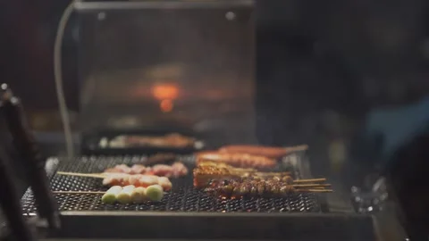 Slow motion of skewers roasting on open grill with smoke at night yatai Japan Stock Footage 321361274