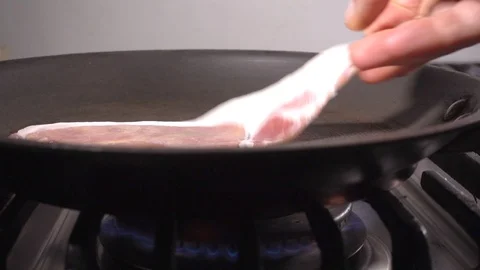 Slow motion: Slice of bacon being placed in a pan. Video stock 89616647