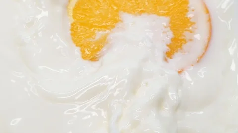Slow motion slice of orange fruit falling down into a bowl of milk Stock Footage