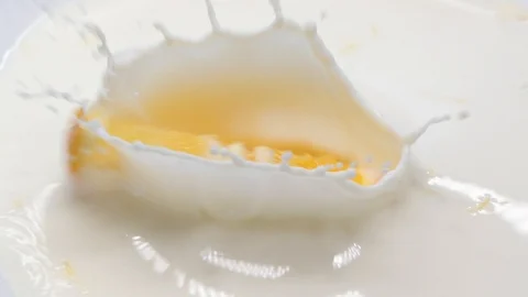 Slow motion slice of orange fruit falling down into a bowl of milk Stock Footage 123511102