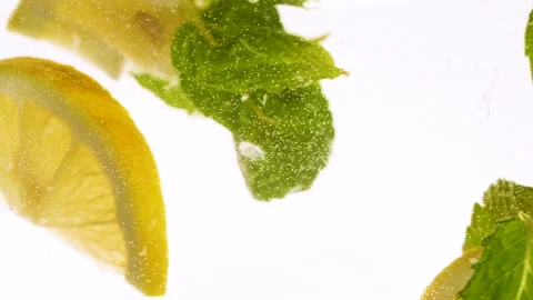 Slow motion slices of lemon or orange fruit and mint leaves splashing in water Stock Footage 312207982