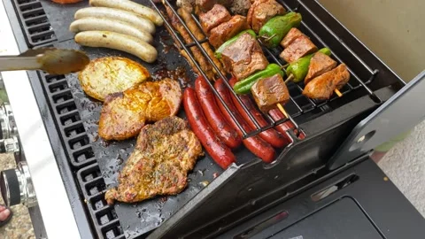 Slow motion slide left shot of tongs turning steak and sausages on BBQ grill in Stock Footage 136736034
