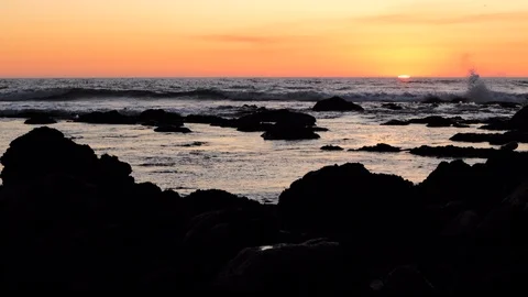 Slow motion slider shot over ocean at sunset, with rocks in foreground Stock Footage 115863519