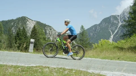 SLOW MOTION: Smiling cyclist easily riding uphill on electric bike in the summer Stock Footage 86623804