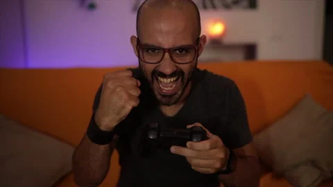Slow Motion: smiling man plays a video game on the sofa having fun. Winner sign Stock Footage 136393774