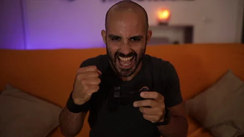 Slow Motion: smiling man plays a video game on the sofa having fun. Winner sign Stock Footage 136393899