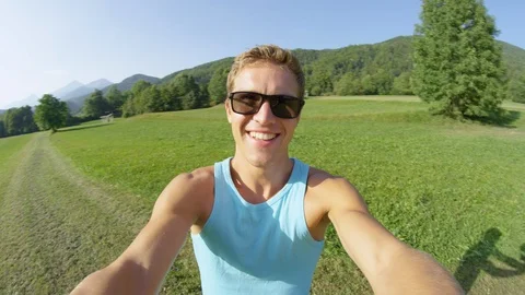 SLOW MOTION: Smiling man wearing sunglasses spins around the sunny meadow. Stock Footage 102592468