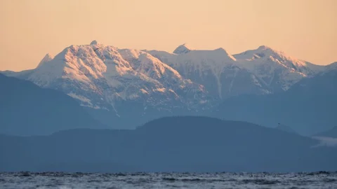 Slow motion snow covered mountain behind ocean with birds flying Stock Footage 128407985