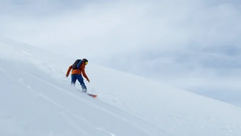 Slow motion of snowboarder riding down steep mountain side in rocky terrain Stock Footage 121597552