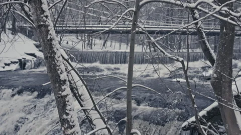 Slow-Motion Snowfall Over Rushing Winter Waterfall next to a Bridge. Version 2 Stock Footage 300022598