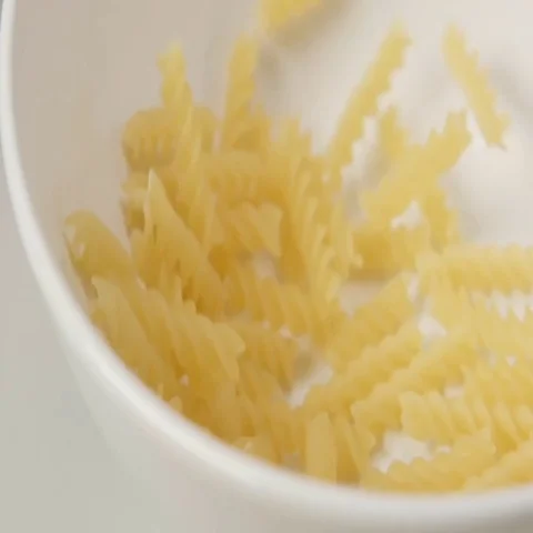 SLOW MOTION: Spiral macaroni fall on white dish (close up) Vídeo Stock 69477037