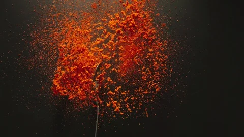 SLOW MOTION: Spoon with red pepper powder falling onto a black table Video stock 107932664