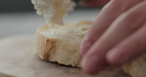 Slow motion spread cream cheese on fresh baguette slice on olive board closeup Video stock 162629282