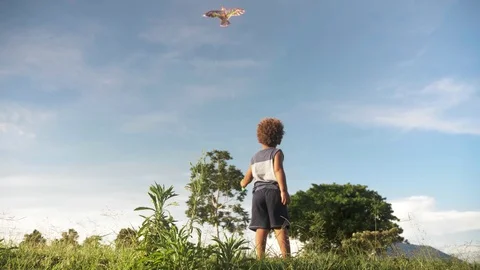 Slow motion still shot from down low behind a young boy flying a kite in Stock Footage 108473390
