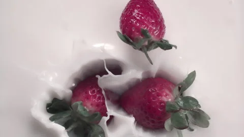Slow motion: Strawberries dropping into milk or cream with a splash. UHD25p Stock Footage 249604482