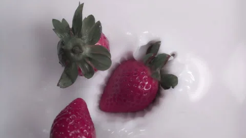 Slow motion: Strawberries dropping into milk or cream with a splash. UHD25p Stock Footage 249604563