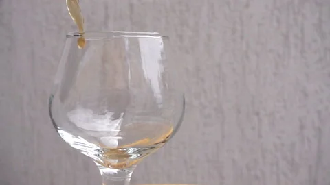 Slow motion a stream of brandy pours into an empty wine glass. Stock Footage 118737197