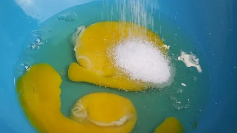 Slow motion sugar falling on egg in blue bowl Stock Footage 310030447