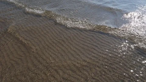 Slow motion sunlit lake water and wave with rippled sand pattern below. Stock Footage
