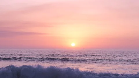 Slow motion sunset over ocean with waves breaking in foreground and yacht Stock Footage 115918911