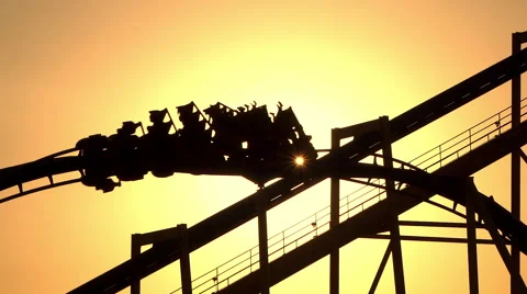 SLOW MOTION: Sunset sun shining through extreme roller coaster ride Stock Footage 62055703