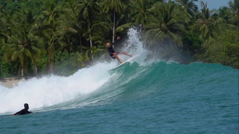SLOW MOTION: Surfer riding a powerful wave with palms trees in the background Stock Footage 333125888