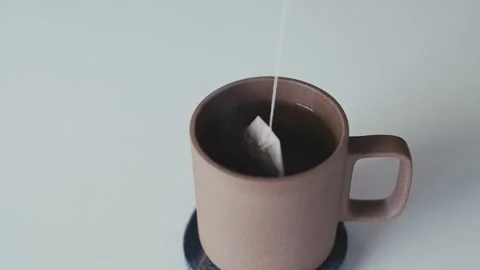 Slow motion tea bag dipped into hot water in a ceramic tea cup Video stock 165767038