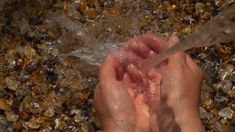 Slow motion of thick jet waterfall and splash on woman hands on pebble beach Stock Footage 98103055
