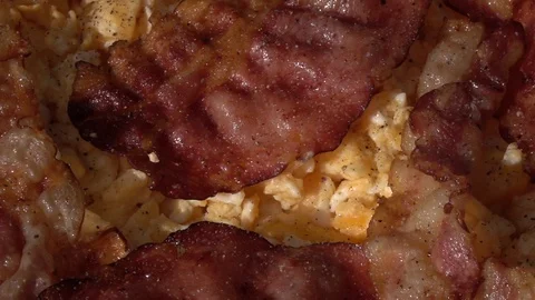 Slow motion of thick peppering scrambled eggs and sliced crispy wavy bacon Stock Footage 99851943