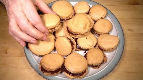 Slow motion – Three hands each choosing a freshly baked macaron from a plate. Stock Footage 104358066