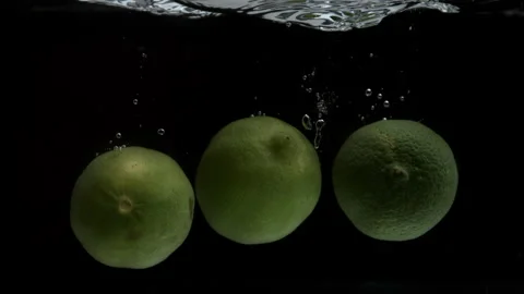 Slow Motion of Three Limes Falling Into a Pool of Water with a Black Backdrop Stock Footage 270407563