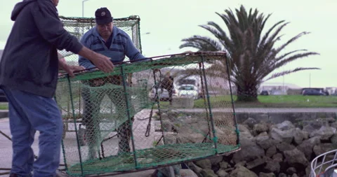 Slow motion of three men taking out empty fish cage from water on cloudy day Video stock 158646572
