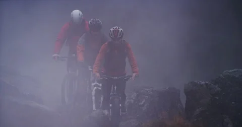 Slow motion through smoke of three mountain bikers peddling toward the camera Vídeo Stock 64688355