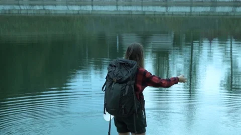Slow motion of throwing stones to the mountain lake by young hipster lady while Video stock 102281983