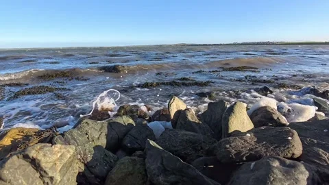 Slow motion tide waves lap towards coastal rocky blue sky beach 스톡 동영상 324964685