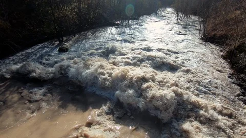 Slow motion tilt down brown wild chaotic dirty water flood river banks Stock Footage 121679970