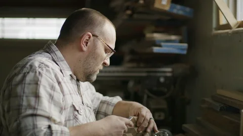 Slow motion tilt down to man chiseling edge of wood with cube pattern / Provo, Stock Footage 89186976