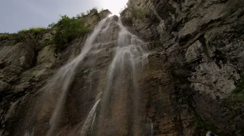 Slow motion tilt pan of waterfall coming down rocky mountainside Video stock 52499062