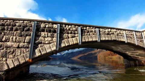 Slow motion tilt up stone arch bridge flooded rapid river leaving Bohinj lake Stock Footage 120690876
