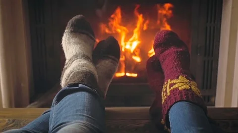 Slow motion toned video of couple warming feet in woolen socks at fireside Stock Footage